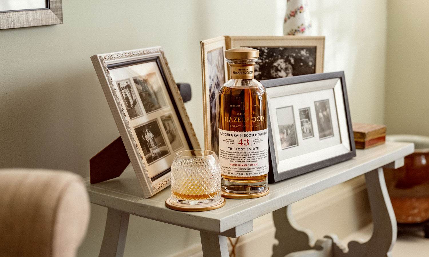 The Lost Estate bottle on a table in front of pictures, next to a glass.