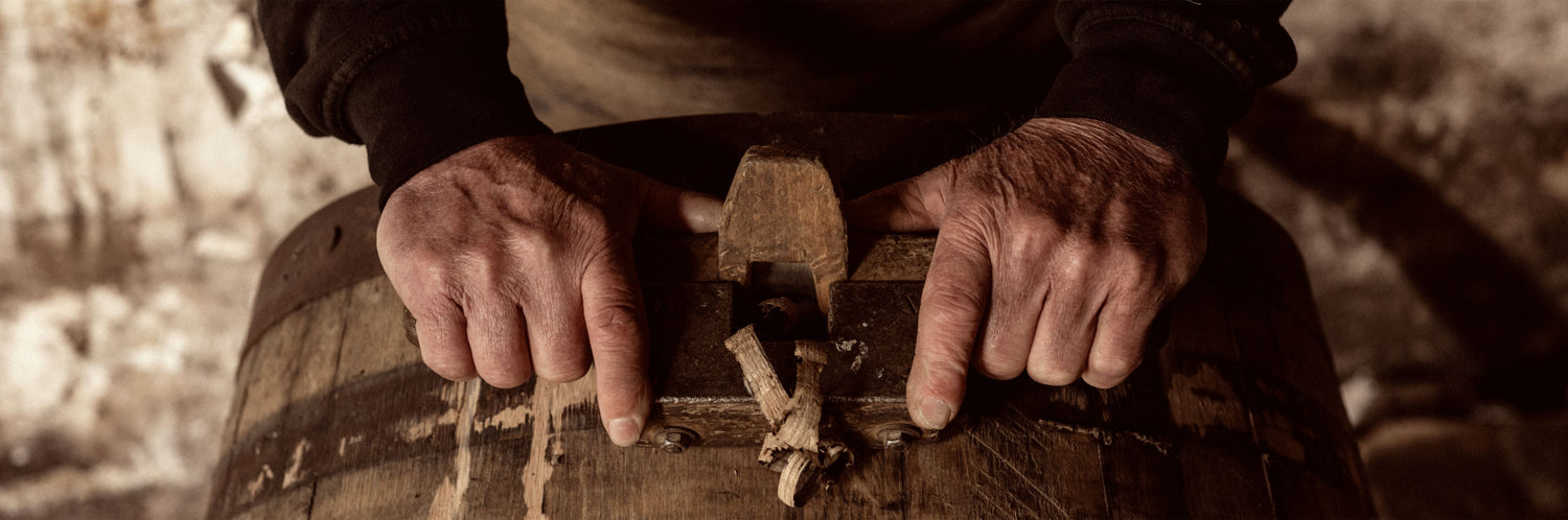 Barrel maker's hands shaving wood off of a barrel.