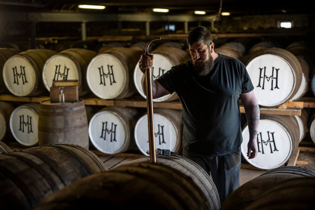 Whisky maker testing whisky in a barrel.