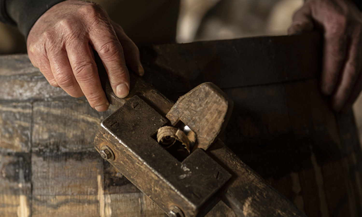 Close up shot of a barrel maker's hands shaving off wood from a barrel.